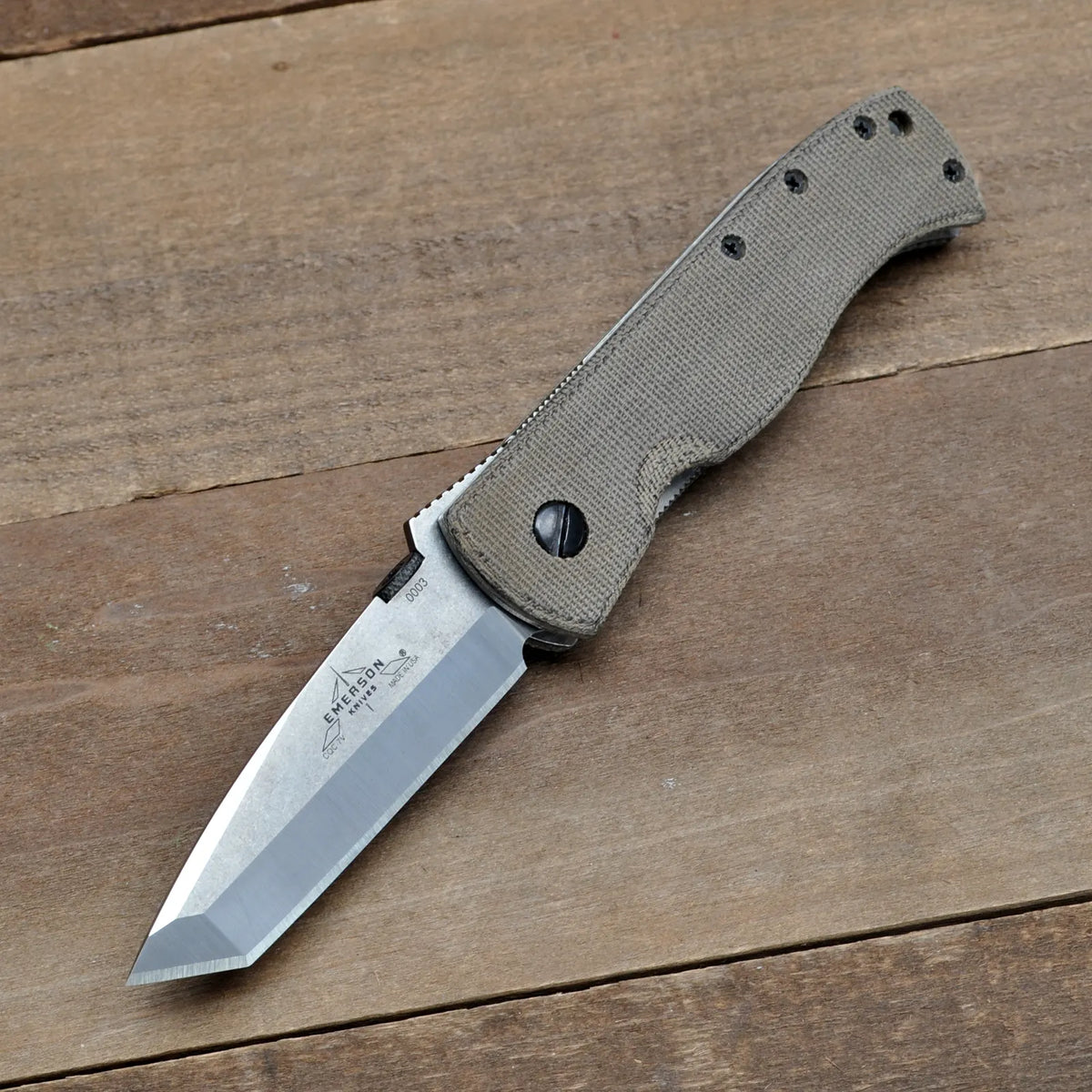 An Emerson Knives, Inc. CQC-7V-SF-NW with an OD Green Micarta handle and silver tanto blade (Serial 0003) lies open on a wooden surface. This item is Final Sale.