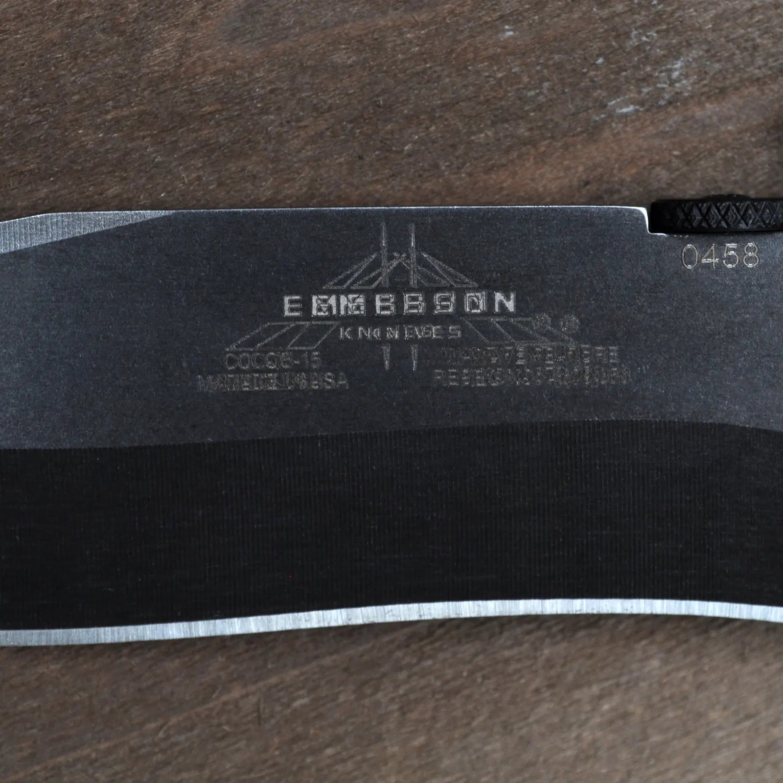 The Emerson Knives, Inc. CQC-15 TF Double Struck, featuring a black textured handle and partially serrated angular blade, is open on a wooden surface. This item is a Final Sale.
