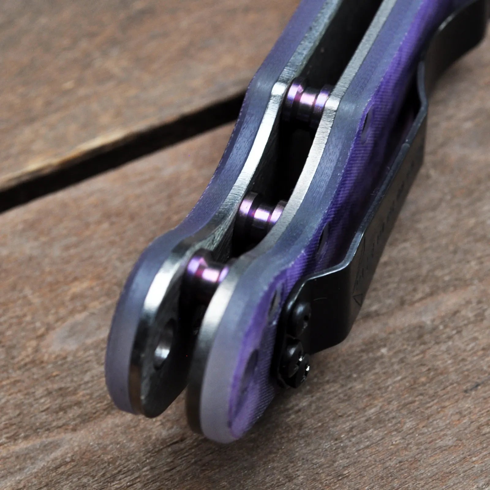 The Elvia NW SF Purple Haze Bling by Emerson Knives, Inc.—a folding karambit with a curved silver blade and purple marbled handle—lies open on wood. Available now as a Final Sale.