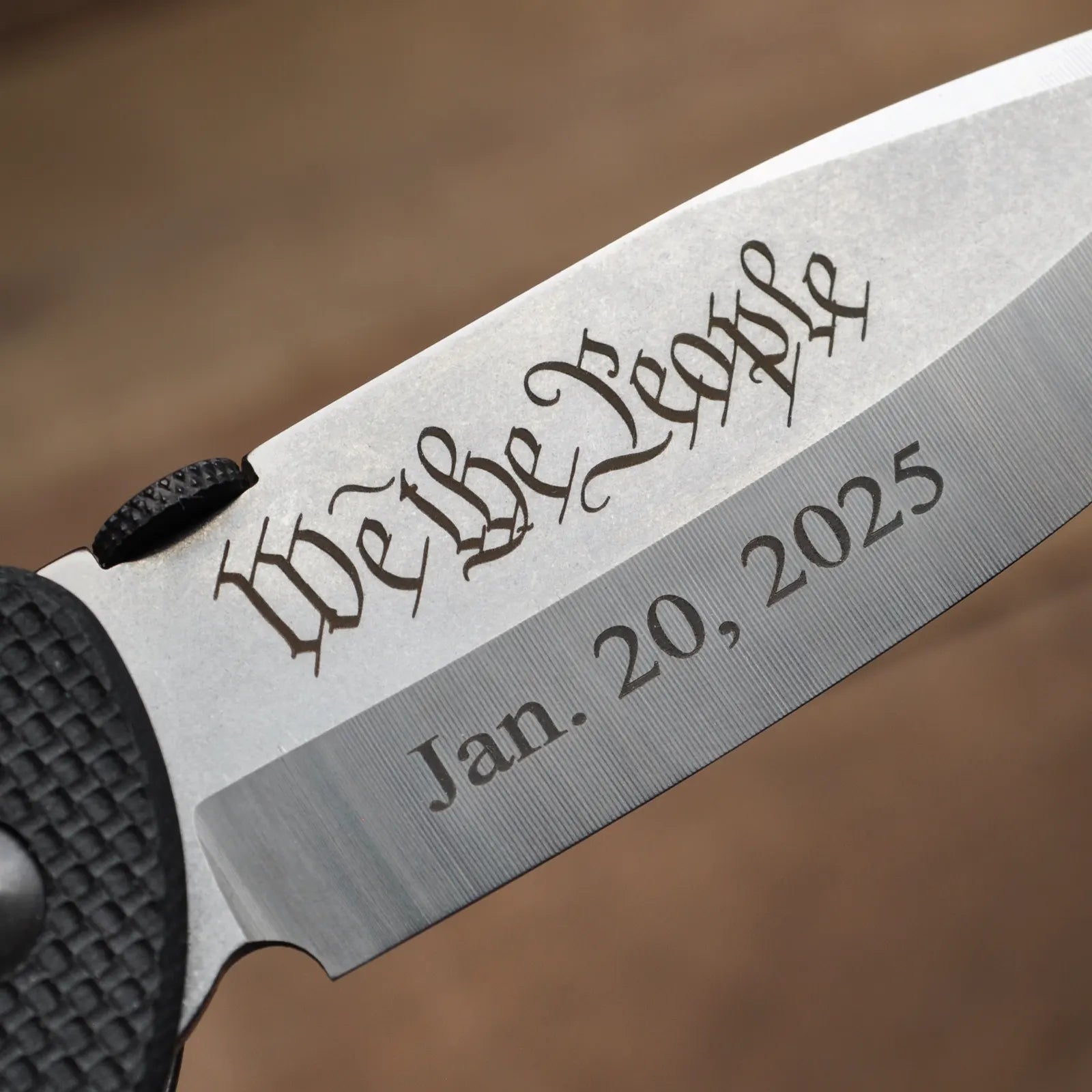 The All American A SF Black Flag Handles with Engraving by Emerson Knives, Inc. is a black folding pocket knife with a textured handle and partially open blade, shown on wood. Available as a final sale item.