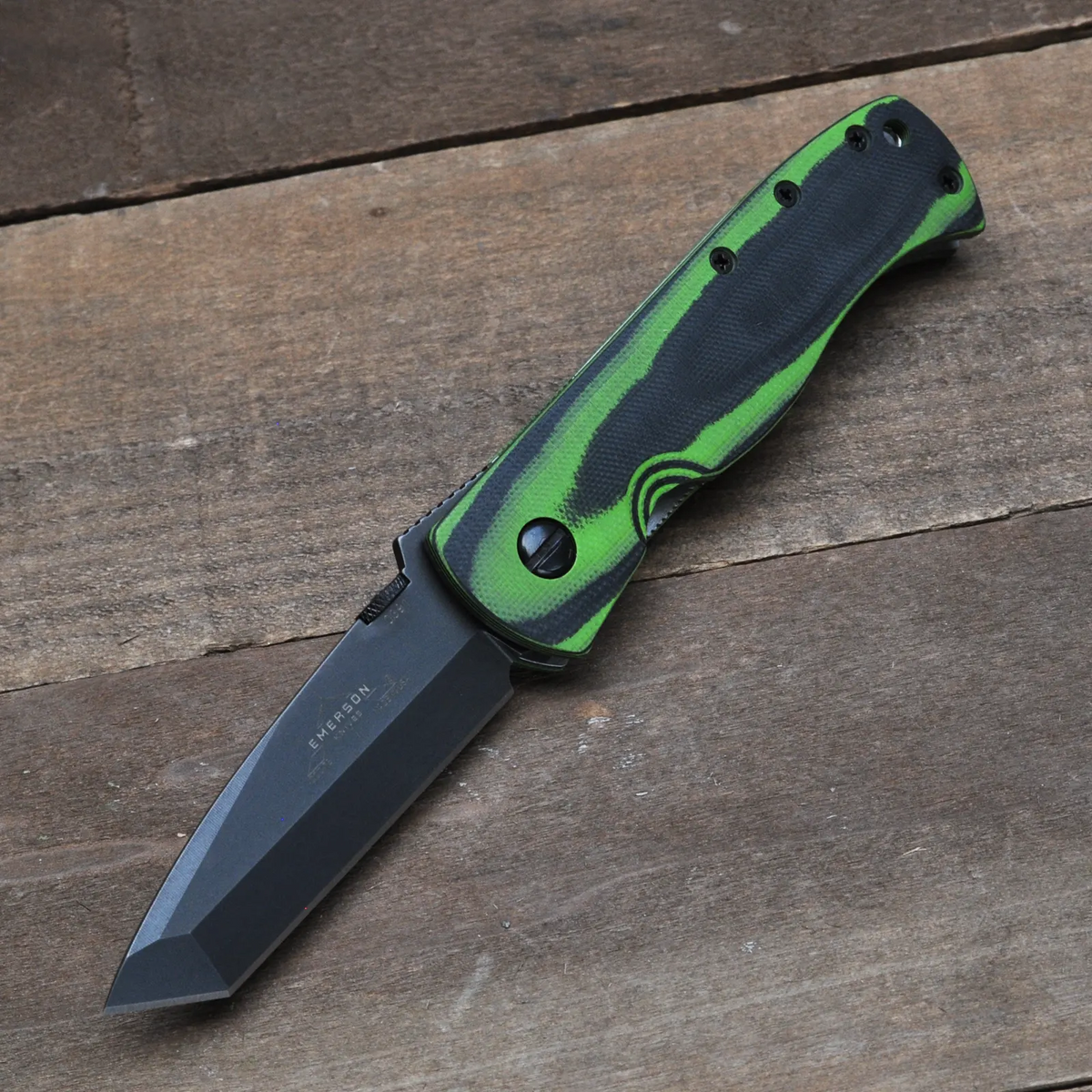 The Emerson Knives, Inc. CQC-7B-NW features a black tanto blade and textured black and green G-10 handle. Shown on wood, it’s part of our Limited Edition Christmas Knives collection. Final Sale item.