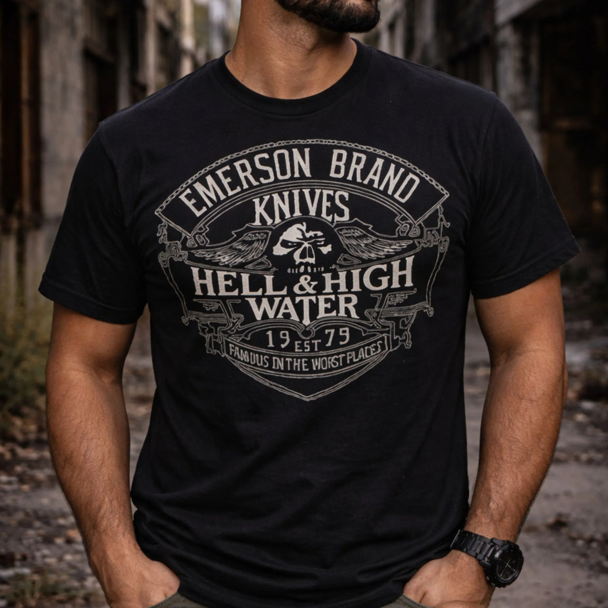 A man stands alone in an urban setting wearing the Emerson Knives, Inc. Hell and High Water T-Shirt, featuring a vintage 1979 graphic on the front.