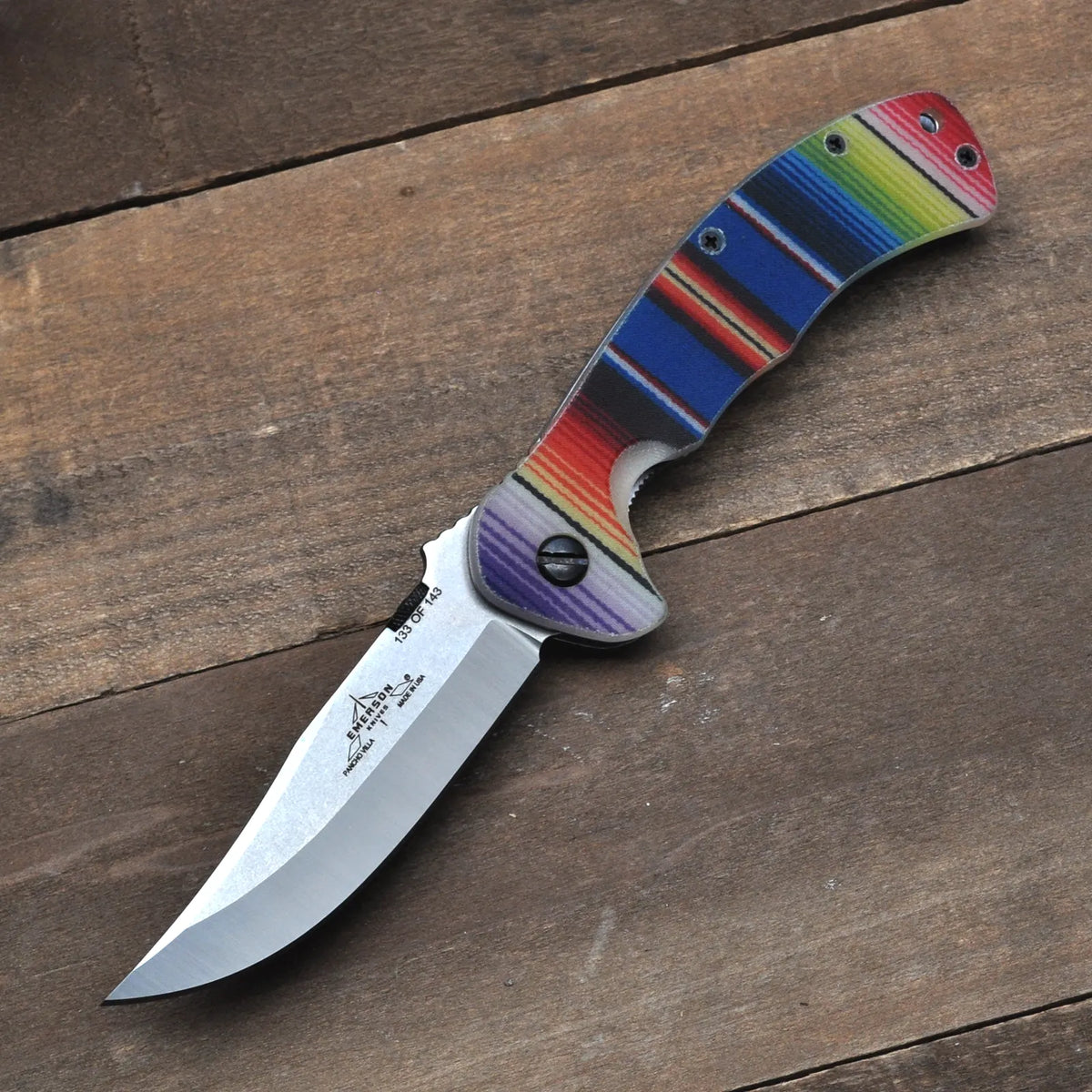 The Pancho Villa Serape G-10 by Emerson Knives, Inc. features a silver blade and colorful striped handle—an eye-catching Limited Edition Final Sale for Christmas Knives collectors, displayed on a wooden surface.