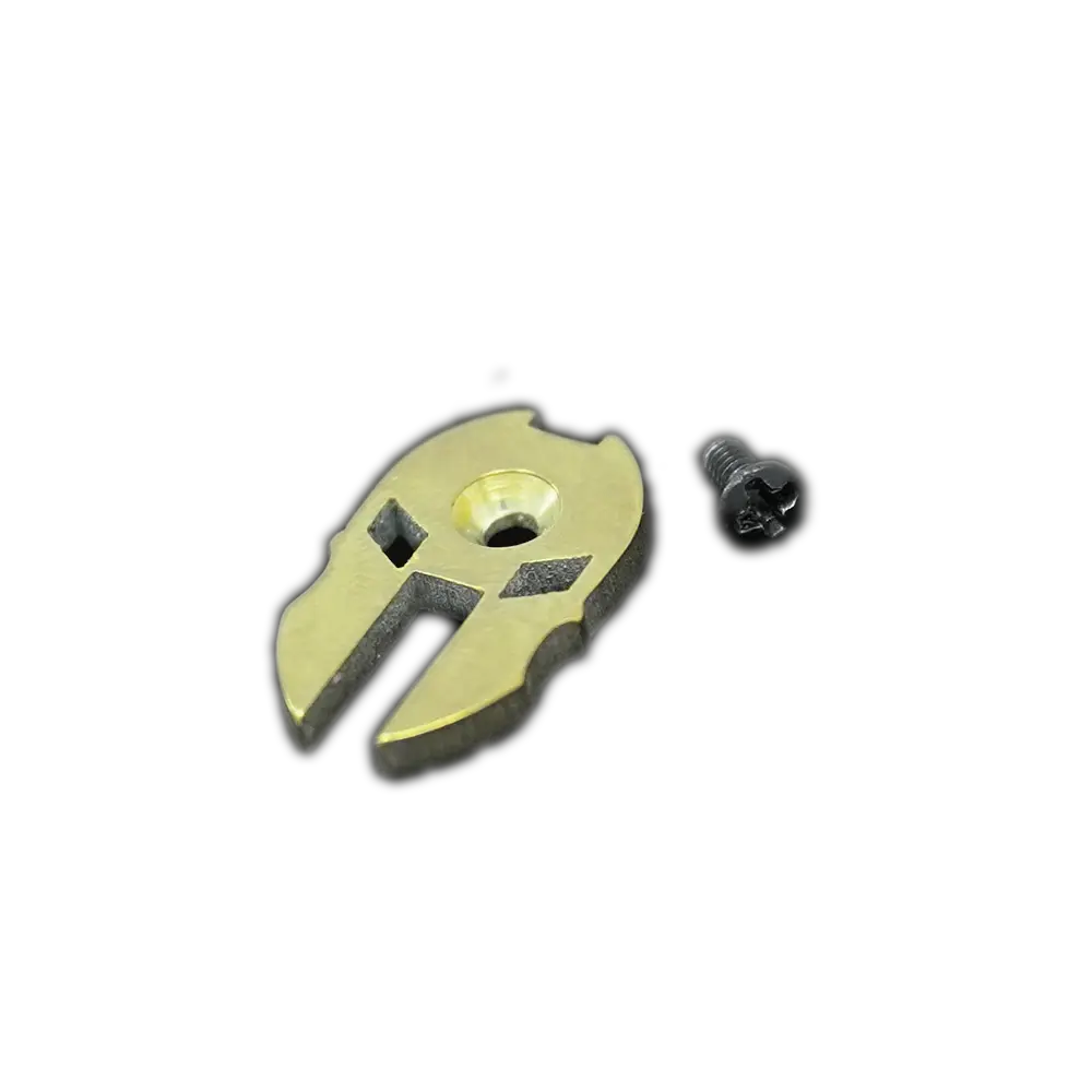 A small, irregularly shaped black Spartan Helmet Thumb Button by Emerson Knives, Inc., with a central hole and markings, lies beside a tiny silver Phillips-head screw on a plain white background.